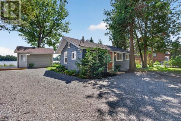 Exterior of a small blue cottage with a gravel driveway and detached garage. - 154 A/b North Beaver Lake Road, Stone Mills