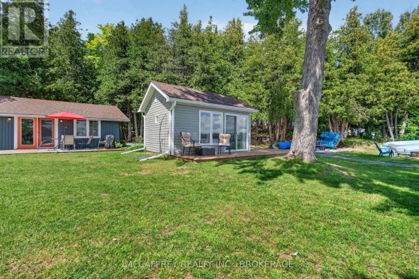 Back view of a grey cottage with a wooden deck facing Beaver Lake and a dock. - 154 A/b North Beaver Lake Road, Stone Mills