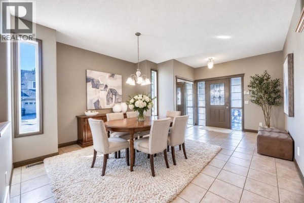 Dining room with a wooden table, upholstered chairs, a shaggy rug, and large windows. - 154 Cranleigh Bay Se, Calgary