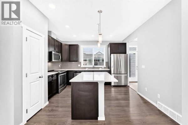 Modern kitchen with dark wood cabinets, stainless steel appliances, and a white island. - 154 Livingston Avenue Ne, Calgary