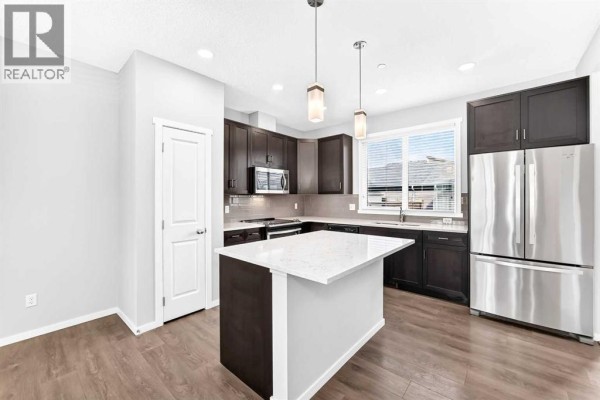 Kitchen with dark wood cabinetry, a white quartz island, stainless steel appliances, and hardwood floors. - 154 Livingston Avenue Ne, Calgary