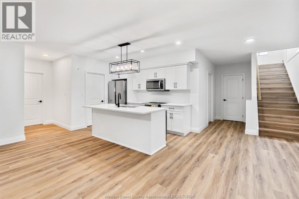 Open concept lower level with a white island kitchen, stainless steel appliances, and stairs. - 154 Mclellan Avenue Unit# B (lower), Amherstburg
