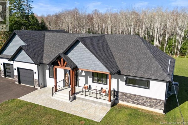 View of the side and front of the house, highlighting the gray roof, white siding, stone base, and covered entrance. - 154 Pit Melanson Cross Road, Saint Antoine