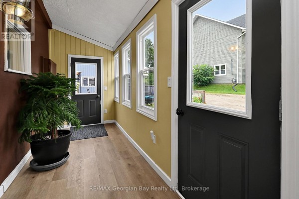 Sunroom with yellow walls, wood-look floor, black doors, and large windows. - 154 Robert Street W, Penetanguishene