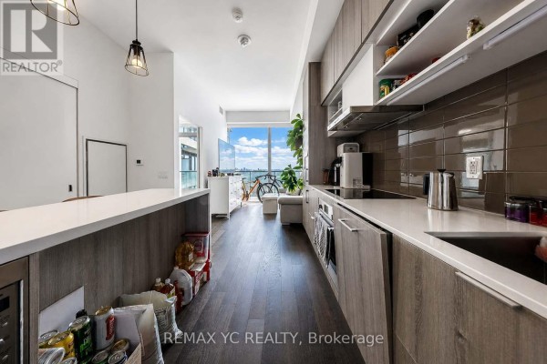 View of a living area and balcony overlooking trees and city buildings through a large window. - 1540 - 8 Hillsdale Avenue E, Toronto