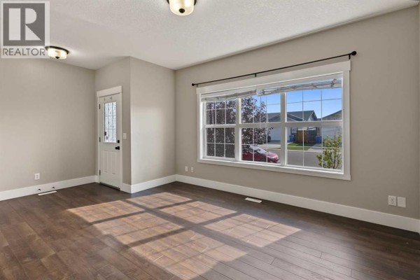 Living room with hardwood floors, a large window, and a white front door. - 1540 Mcalpine Street, Carstairs