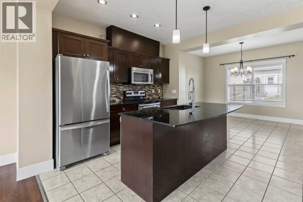 Kitchen with dark wood cabinets, granite island, stainless steel appliances and tile floor. - 1540 Mcalpine Street, Carstairs