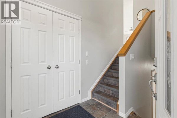 Interior entryway with light grey walls, white bi-fold doors, and a stairwell with dark tile treads. - 1541 Big Springs Way Se, Airdrie
