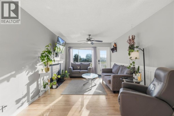 Living room with grey walls, a white fireplace, a grey sofa, a beige armchair, and a large window view. - 1541 Big Springs Way Se, Airdrie
