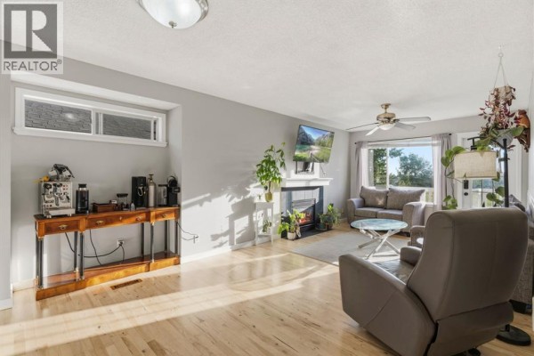 Living room with a fireplace, a grey sofa, a reclining armchair, and a wooden console table with an espresso machine. - 1541 Big Springs Way Se, Airdrie