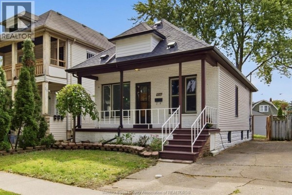Side exterior view of a white brick house with a covered front porch and burgundy trim. - 1541 Lincoln Road, Windsor