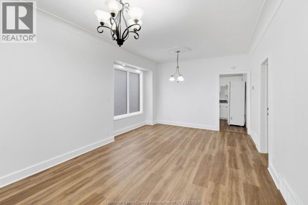 Empty living and dining area with white walls, wood floors, and chandelier lighting. - 1541 Lincoln Road, Windsor