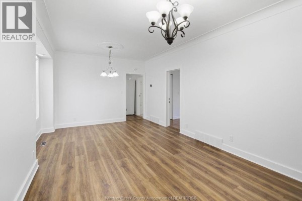 Empty living and dining area with white walls, wood floors, and two chandelier lights. - 1541 Lincoln Road, Windsor