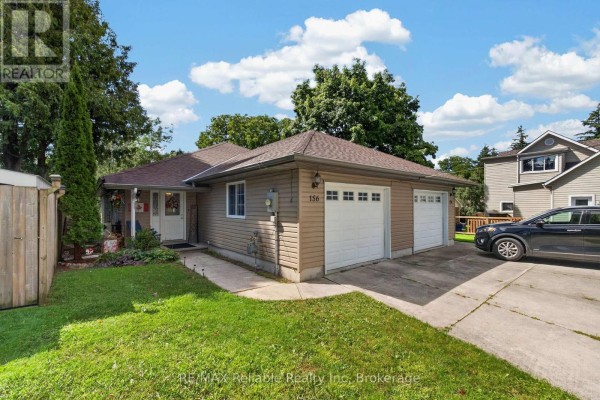 Front view of a duplex with two garage doors, tan siding, and a green lawn on a sunny day. - 154&156 Princess Street E, Central Huron