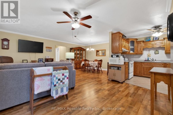 Open-concept living area with a grey sofa, dining table, and wooden kitchen cabinets and flooring. - 154&156 Princess Street E, Central Huron
