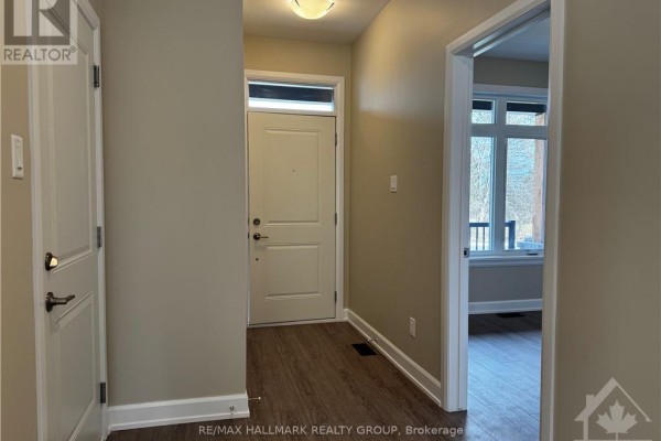 Interior view of a townhouse foyer with a white front door, wood-look flooring, and an adjacent doorway. - 1543 Flanders Road, Brockville