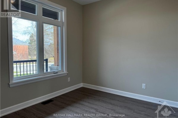 Interior view of a room with a large window overlooking the street, beige walls, and dark wood-look flooring. - 1543 Flanders Road, Brockville