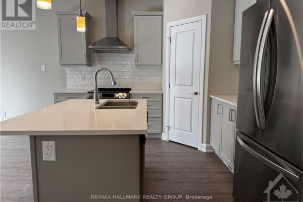 Close-up view of a modern kitchen with gray cabinets, a stainless steel refrigerator, and a white subway tile backsplash. - 1543 Flanders Road, Brockville