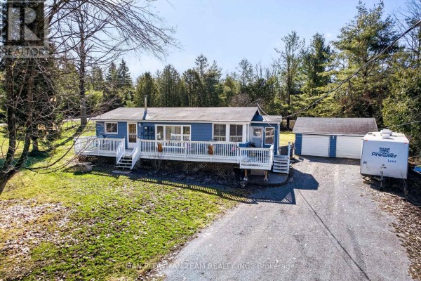 Aerial view of a blue house, detached garage, and trailer on a wooded property. - 1545 Westview Crescent, Selwyn