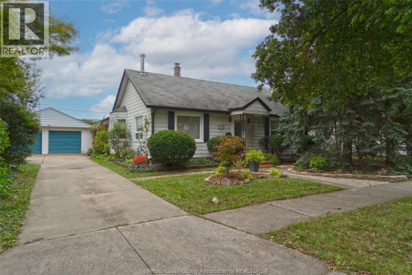Side view of a white bungalow showing the front lawn, garden beds, and detached garage. - 1546 California Avenue, Windsor