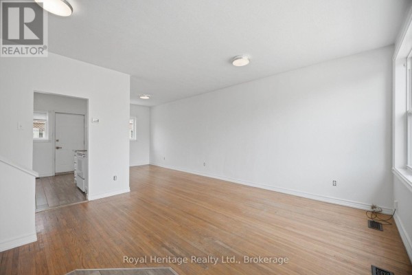 Open-concept living and dining area with a large window, hardwood floors, and a wooden table. - 1546 Lakemount Street, Oshawa