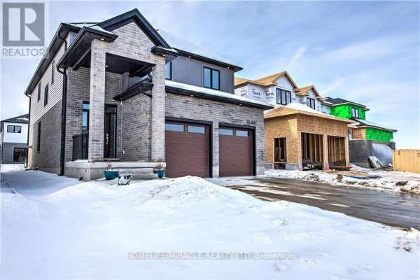 Side view of the brick house with a covered entrance and two garage doors, construction next door. - 1546 Medway Park Drive, London North