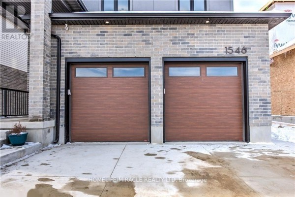 Close-up of two wood-look garage doors with windows on the front of a brick house. - 1546 Medway Park Drive, London North