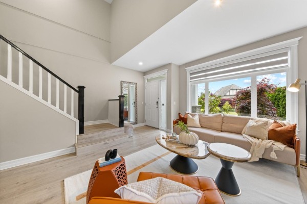 Living room and entryway with beige sofa, marble coffee table, orange armchair, and view of backyard and staircase. - 15460 36a Avenue, Surrey