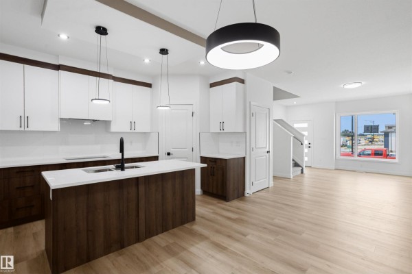 Modern kitchen with white countertops, dark wood lower cabinets, white uppers, and an island with pendant lights. - 1547 211 St Nw, Edmonton