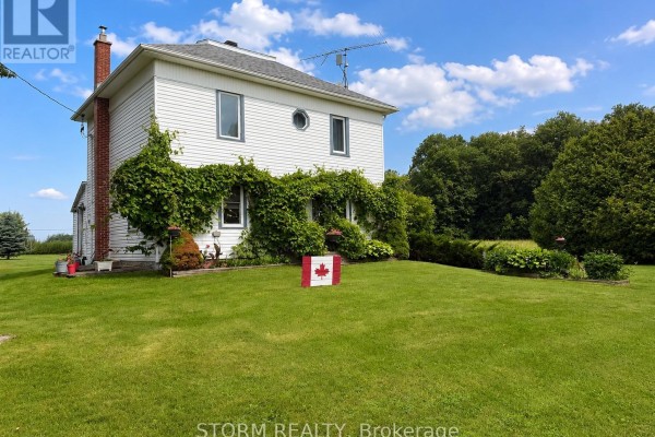Front view of a white two-story house with a white door and green ivy covering the entrance. - 15477 Raymond Road, South Stormont