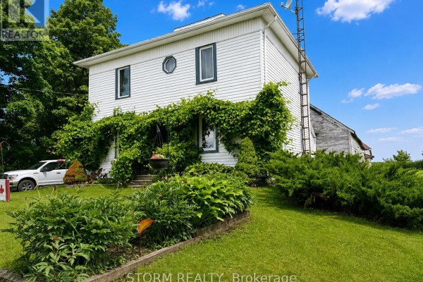Side view of a white house with a brick chimney, green ivy, and an attached barn. - 15477 Raymond Road, South Stormont