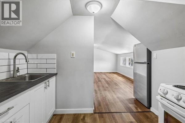 Interior view of a small kitchen with white cabinets and a sink, opening to a living area. - 155 1/2 Lake Street, St  Catharines