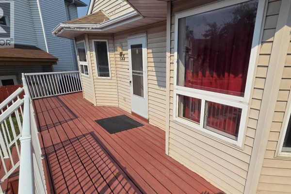 Close-up of the red deck with white railings, beige siding, and large windows with red curtains. - 155 Applefield Close Se, Calgary