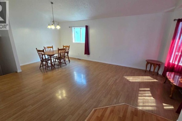 Living and dining room with light wood floors, white walls, a wooden dining table and chairs, and red curtains. - 155 Applefield Close Se, Calgary