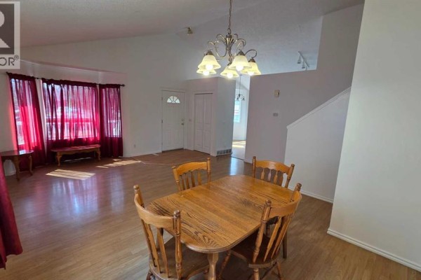 Living and dining room with light wood floors, white walls, a wooden dining table and chairs, and large bay windows. - 155 Applefield Close Se, Calgary