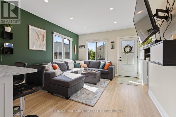 Grey sectional sofa, breakfast bar, and wall-mounted TV in a modern living room - 155 Broadway Street Welland