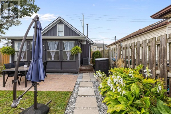 Brick patio with dining set and umbrella next to a stone path and flower beds - 155 Broadway Street Welland