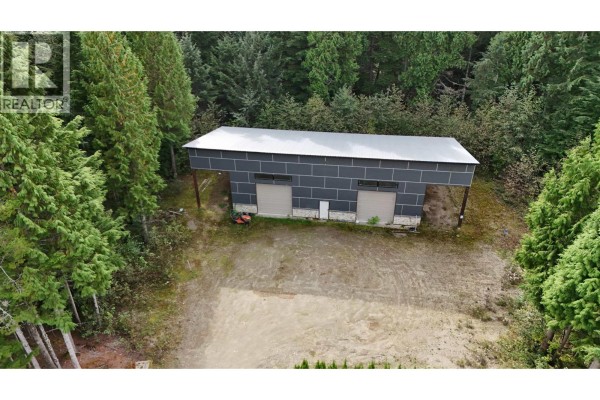 Exterior of a grey metal building with two garage doors situated in a wooded area. - 155 Dewberry Street, Kitimat