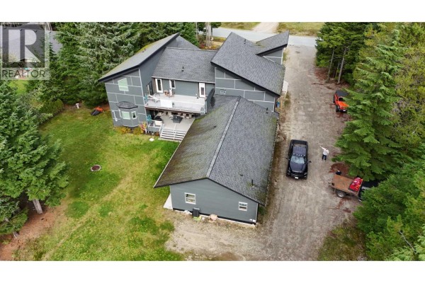 Rear aerial view of the grey residential house showing a deck, garage, and driveway. - 155 Dewberry Street, Kitimat