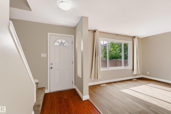 Interior entryway with a white door, staircase, and adjoining living area. - 155 Primrose Gardens Gd Nw, Edmonton