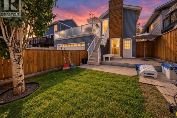 Backyard with a green lawn, wooden fence, deck, stairs, and a detached garage. - 155 Strathcona Close Sw, Calgary