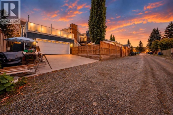 Gravel driveway leading to a detached double garage with a wooden fence on the right. - 155 Strathcona Close Sw, Calgary