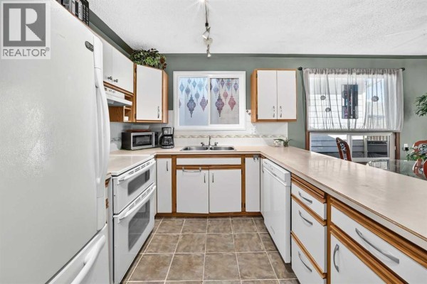 White kitchen with beige tile floors, white appliances, and wooden cabinet trim. - 155 Strathcona Close Sw, Calgary