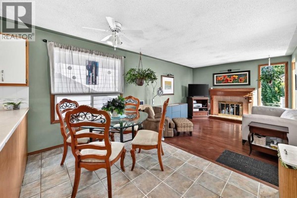 Dining area with a glass table and ornate chairs next to a living room with a fireplace. - 155 Strathcona Close Sw, Calgary