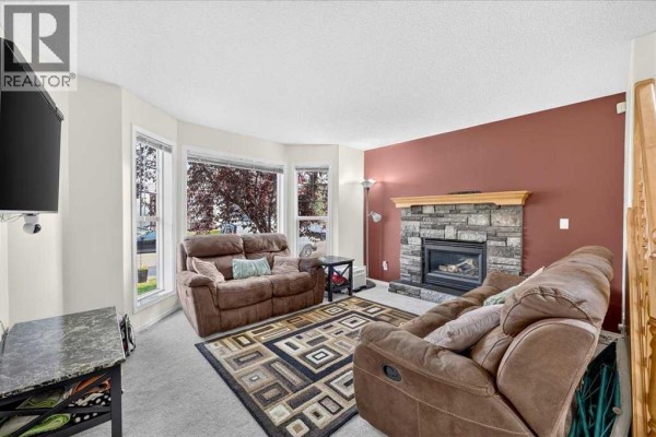 Living room with a stone fireplace, two brown reclining sofas, and a geometric patterned rug. - 155 Tarington Green Ne, Calgary