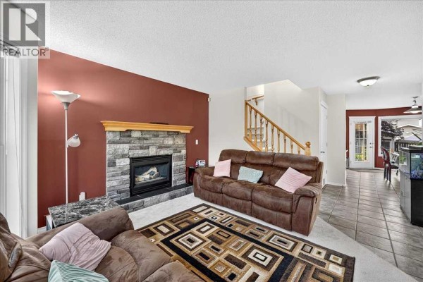 Living room with a stone fireplace, brown sofa, stairs, and view into the dining area and kitchen. - 155 Tarington Green Ne, Calgary