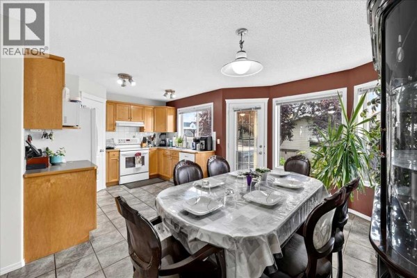 Dining room adjacent to a kitchen with light wood cabinets, table set for six, and large bay windows. - 155 Tarington Green Ne, Calgary