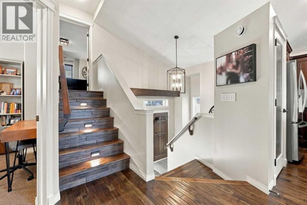 View of a home's interior staircase with wooden steps and lights, leading down to a doorway. - 155 Webster Drive, Red Deer