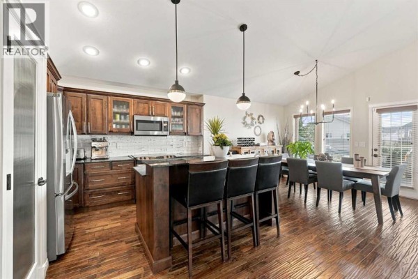 Open-concept kitchen and dining area with wood cabinets, island seating, and a dining table. - 155 Webster Drive, Red Deer