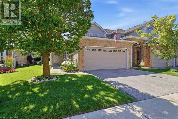 Front exterior of beige brick townhouse with a double garage door. - 1550 Gordon Street Unit# 18, Guelph